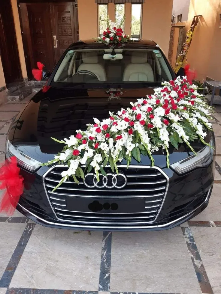 Black car with a red and white flower arrangement across the bonnet