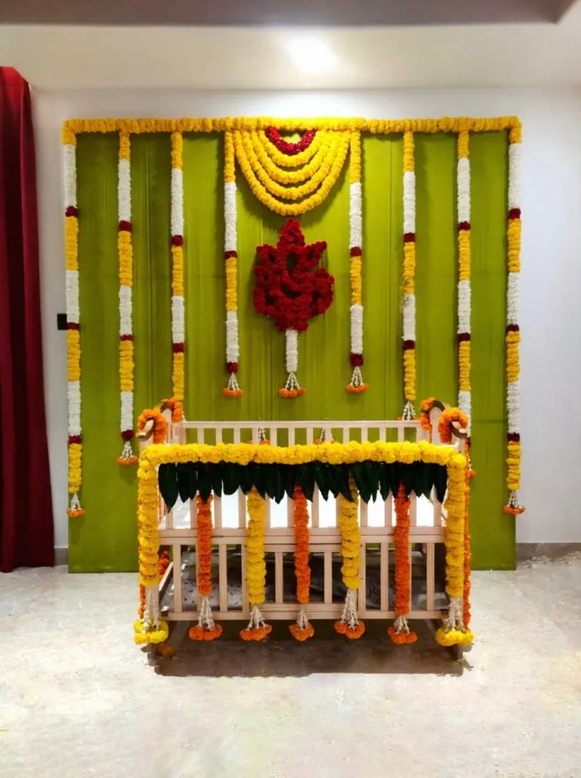 White cradle decorated with marigold flowers before a green floral backdrop