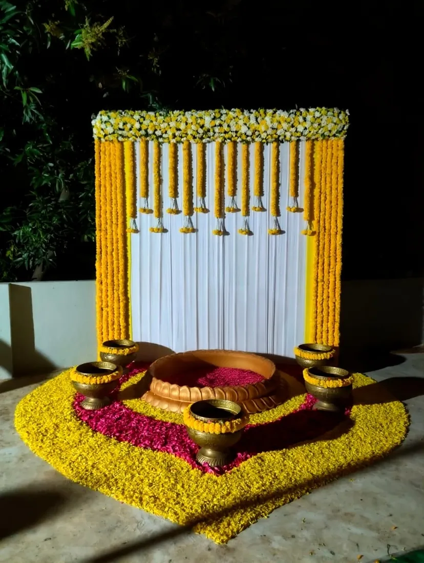 Marigold and pink flower-petal mandala in front of a Mangala Snanam setting