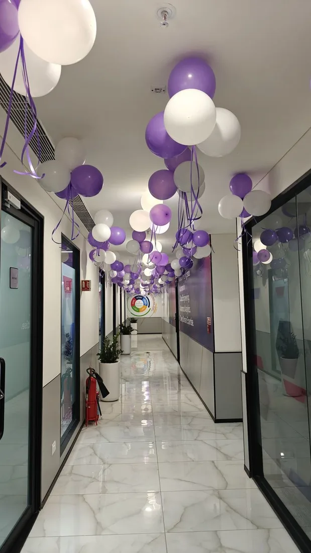Purple and white ceiling balloon clusters with ribbons along an office corridor